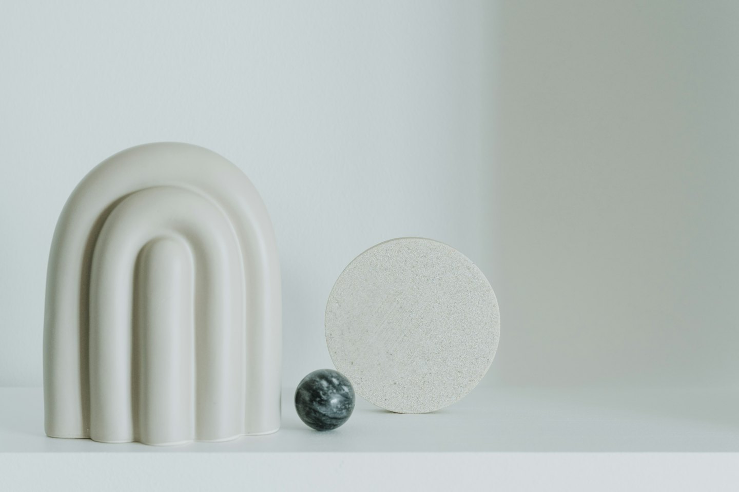 Arco de cerámica color crema, esfera veteada y disco beige sobre un estante.