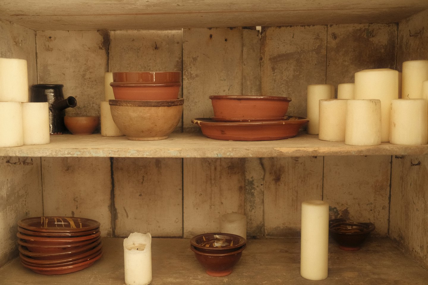 Cerámica artesanal y velas blancas sobre estantes de madera.