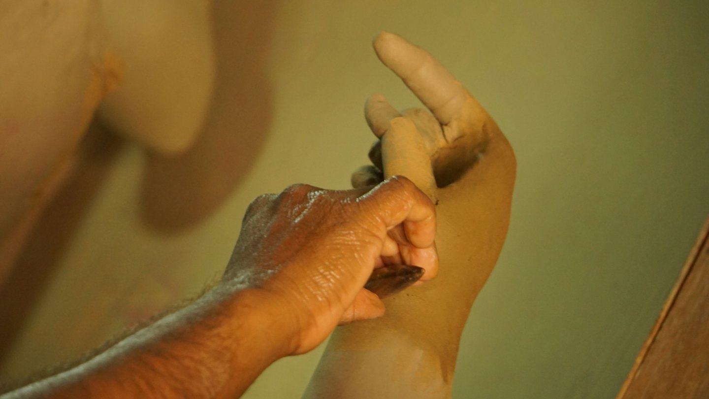 Un artesano da forma a una escultura de arcilla de una mano.