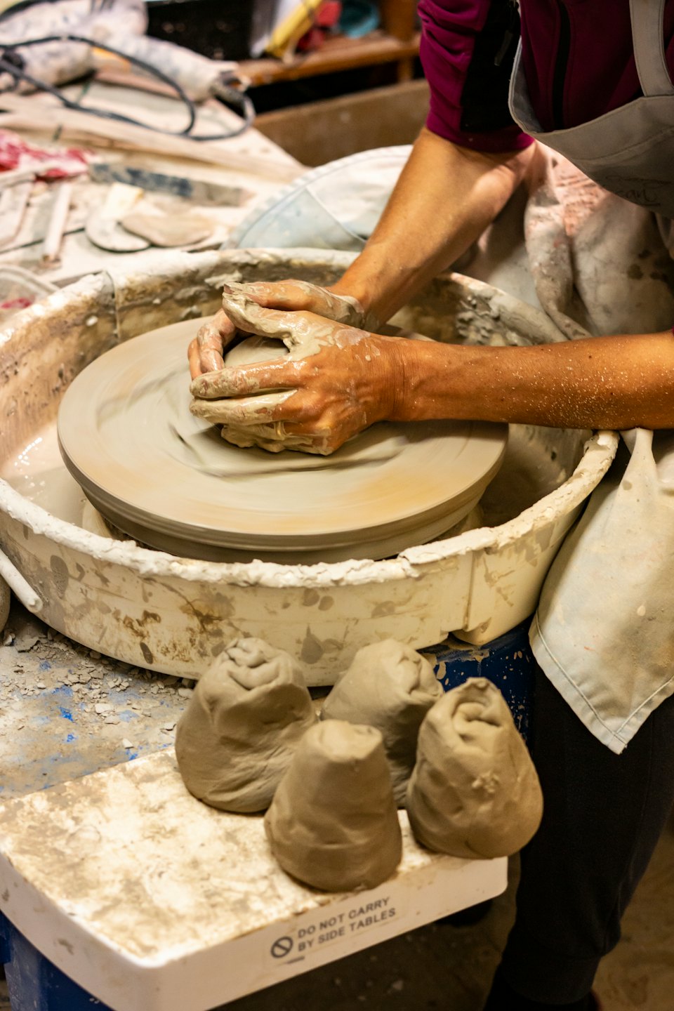 Manos cubiertas de arcilla húmeda dando forma a una vasija en un torno de alfarero.