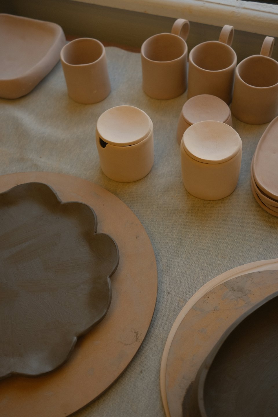 Tazas y recipientes de cerámica de arcilla cruda sobre una mesa de estudio.